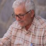 Senior man sitting outdoors against a stone wall, capturing a serene moment in Izmir, Türkiye.